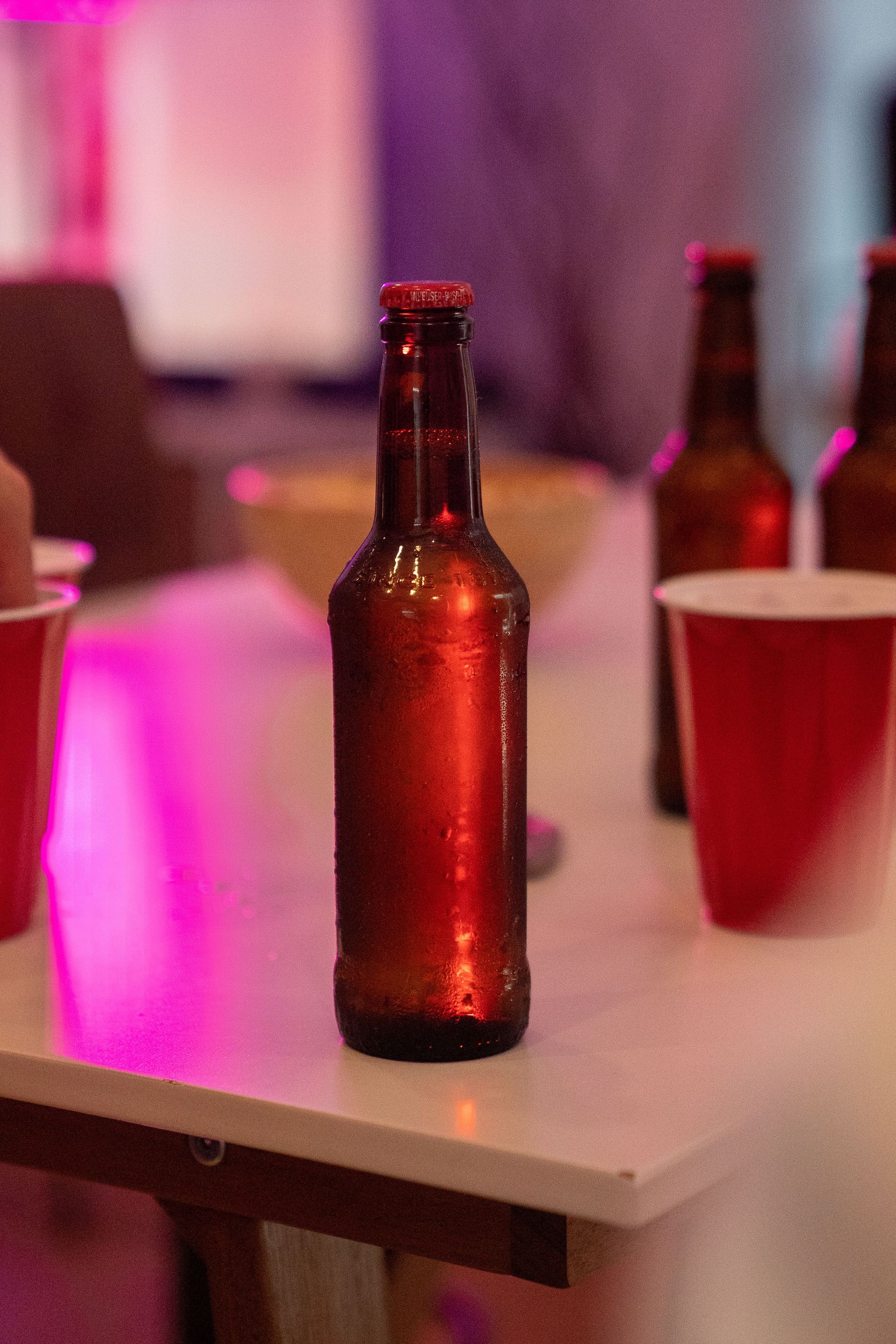 Chilled beer bottle surrounded by red cups on a white table at a party setting.